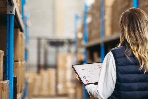Rearview of a logistics manager using a digital warehouse management system on a tablet. Female warehouse employee working with statistical reports on her inventory management dashboard.